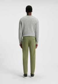 Light grey wool sweater, olive green tapered trousers, and black sneakers with white soles, viewed from the back. Smooth textures and simple design.