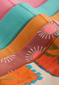 Morceaux de tissu colorés empilés avec des coutures visibles ; les motifs incluent un uni turquoise, moutarde, rose avec des motifs de soleil, et orange avec des accents bleus et verts.