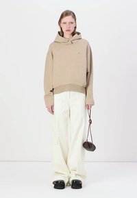 Beige cropped hoodie met een front pocket en een trekkoord, gecombineerd met brede witte broeken en donkere instappers. Kleine bruine handtas.