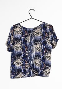Blusa a maniche corte con un motivo geometrico blu, crema e rosa. Realizzata in un tessuto morbido, presenta un dettaglio arricciato sul retro.