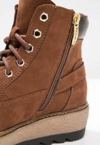 Brązowy zamszowy botek za kostkę z bocznym zamkiem błyskawicznym, metalowymi akcentami, teksturowaną podeszwą środkową i czarną podeszwą gumową dla lepszej przyczepności.