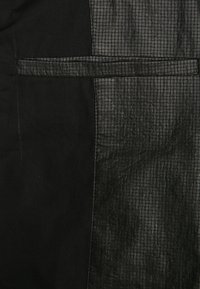 Czarny strój z dwoma teksturami: gładka tkanina z jednej strony i sztuczna skóra w kratkę z drugiej, z poziomym akcentem.