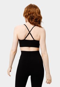 Il bralette nero a coste presenta un design cropped con spalline incrociate regolabili e una texture liscia, abbinato a leggings neri a vita alta.