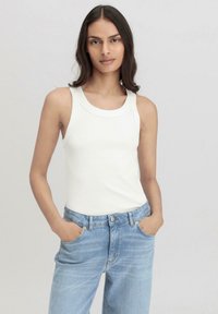 Weißes, geripptes Tanktop mit rundem Ausschnitt, kombiniert mit hellblauen Jeans im Straight-Leg-Stil, die seitliche Taschen und subtile Nähte aufweisen.