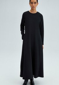 Lang sort kjole med lange ærmer og rund halsudskæring. Lavet af glat stof, med sidelommer og en svævende silhuet.