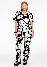 Ensemble ample à motif floral avec une base noire et de grandes fleurs blanches. Le haut a des manches courtes et un col en V; les pantalons sont évasés.