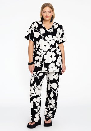 Blumengemustertes, lockeres Outfit mit schwarzem Grund und großen weißen Blumen. Das Oberteil hat kurze Ärmel und einen V-Ausschnitt; die Hose ist weit geschnitten.