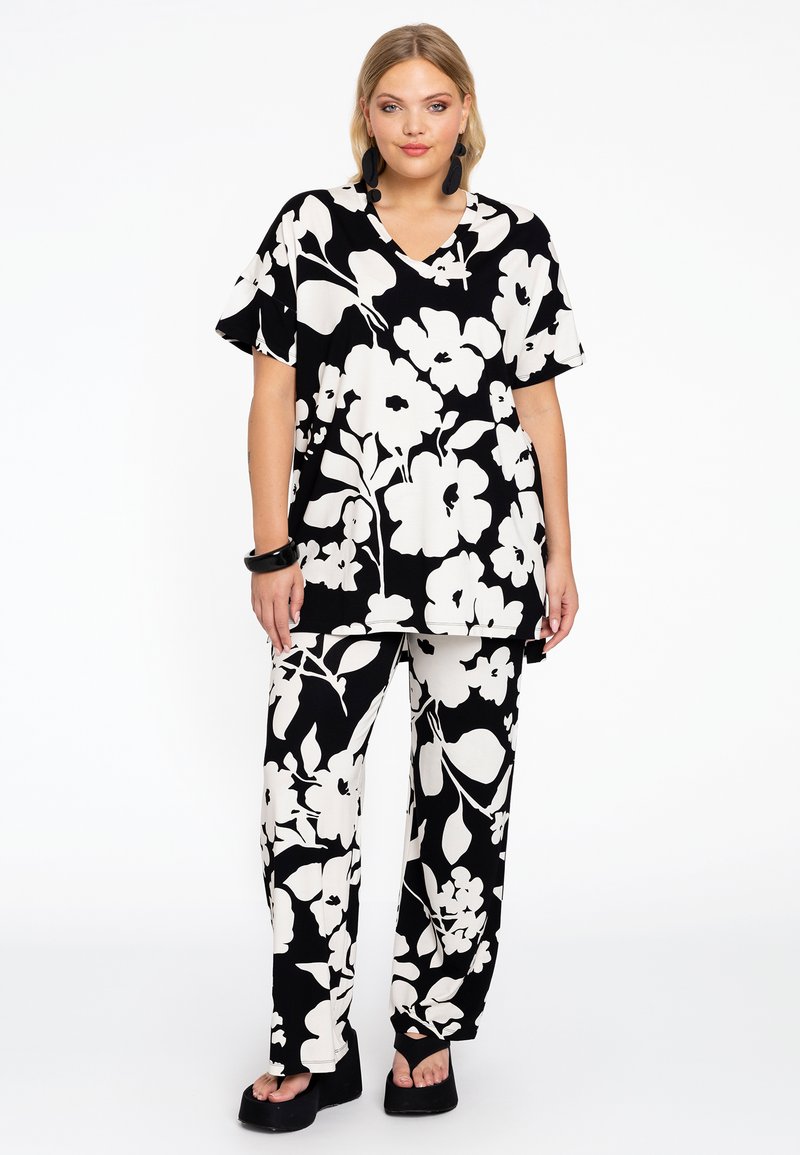 Ensemble ample à motif floral avec une base noire et de grandes fleurs blanches. Le haut a des manches courtes et un col en V; les pantalons sont évasés.