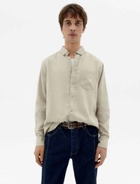 Helle beige Knopfhemd mit einer Brusttasche, kombiniert mit dunkelblauen Jeans und einem braunen Gürtel mit weißen Metallpunkten.