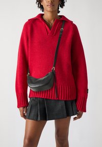 Red knit sweater with a V-neck and ribbed cuffs, paired with a black leather crossbody bag and a plaid pleated skirt.
