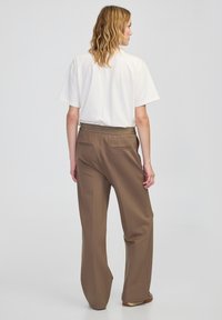 Biała koszula krótki rękaw w zestawieniu z brązowymi spodniami typu wide-leg. Spodnie posiadają teksturowany pas oraz dwie tylne kieszenie.