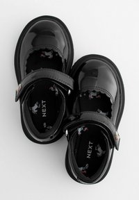 Chaussures Mary Jane en cuir verni noir avec une bride, présentant une doublure noire ornée de licornes colorées. Les semelles en caoutchouc offrent une bonne adhérence.