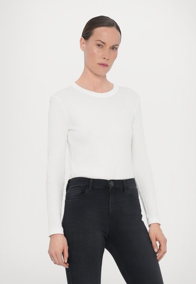 Vit långärmad skjorta i bomull med rund halsringning, kombinerad med svarta jeans. Skjortan har en åtsittande siluett och en mjuk textur.