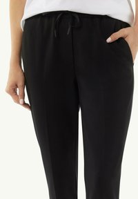 Zwarte tapse broek gemaakt van een zachte stof, met een elastische tailleband met trekkoord, zijzakken en een gladde textuur.