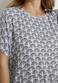 Top in tessuto bianco con un motivo a ventaglio nero e blu, scollo rotondo e maniche corte. Tessuto morbido con una vestibilità comoda.