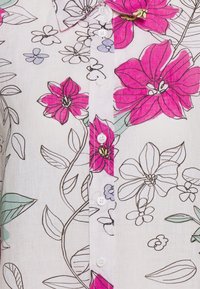 Floral print shirt featuring bold pink flowers and light green leaves on a white linen background. Includes a button-down front and collar.