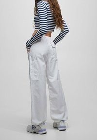 Witte cargo broeken met zijzakken, gecombineerd met een marineblauw en wit gestreepte lange mouwen crop top. Kenmerkt een losse pasvorm en textuurstof.