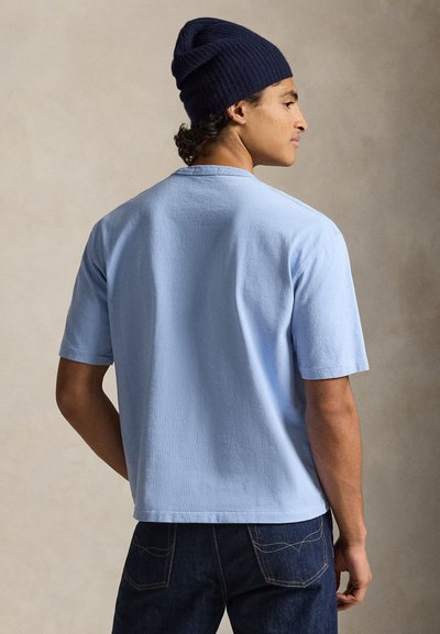 Ανοιχτό μπλε κοντομάνικο T-shirt, από απαλό βαμβακερό ύφασμα με άνετη γραμμή. Φορεμένο με σκουρόχρωμο τζιν και ναυτικό σκουφάκι.