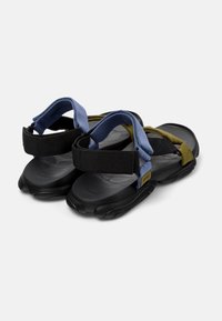 Kaksiväriset sandaalit, joissa on musta kumipohja, siniset ja mustat kangasnauhat vihreillä yksityiskohdilla ja säädettävät Velcro-kiinnitykset.