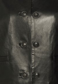 Černá kožená bunda s dvojnásobně zapínaným designem, šesti kulatými černými knoflíky a dvěma bočními kapsami s texturovaným povrchem.