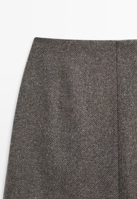 Grauer Wollrock mit Fischgratmuster, ausgestattet mit einer glatten Textur und einem figurbetonten Design. Schlichte Taille ohne sichtbare Beschläge.