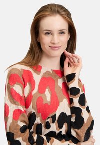 Knit sweater featuring a leopard print pattern in red, black, and beige tones; textured fabric with long sleeves and a round neckline.