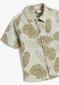 Korte mouwen shirt van lichtgroene stof met een beige tropisch bladerenpatroon, knoopsluiting en een klassieke kraagontwerp.