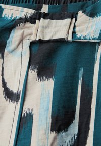 Mehrfarbiger Stoff mit abstrakten Mustern in Türkis, Schwarz und Creme. Glatte Textur mit einem gerafften Taillenbund.