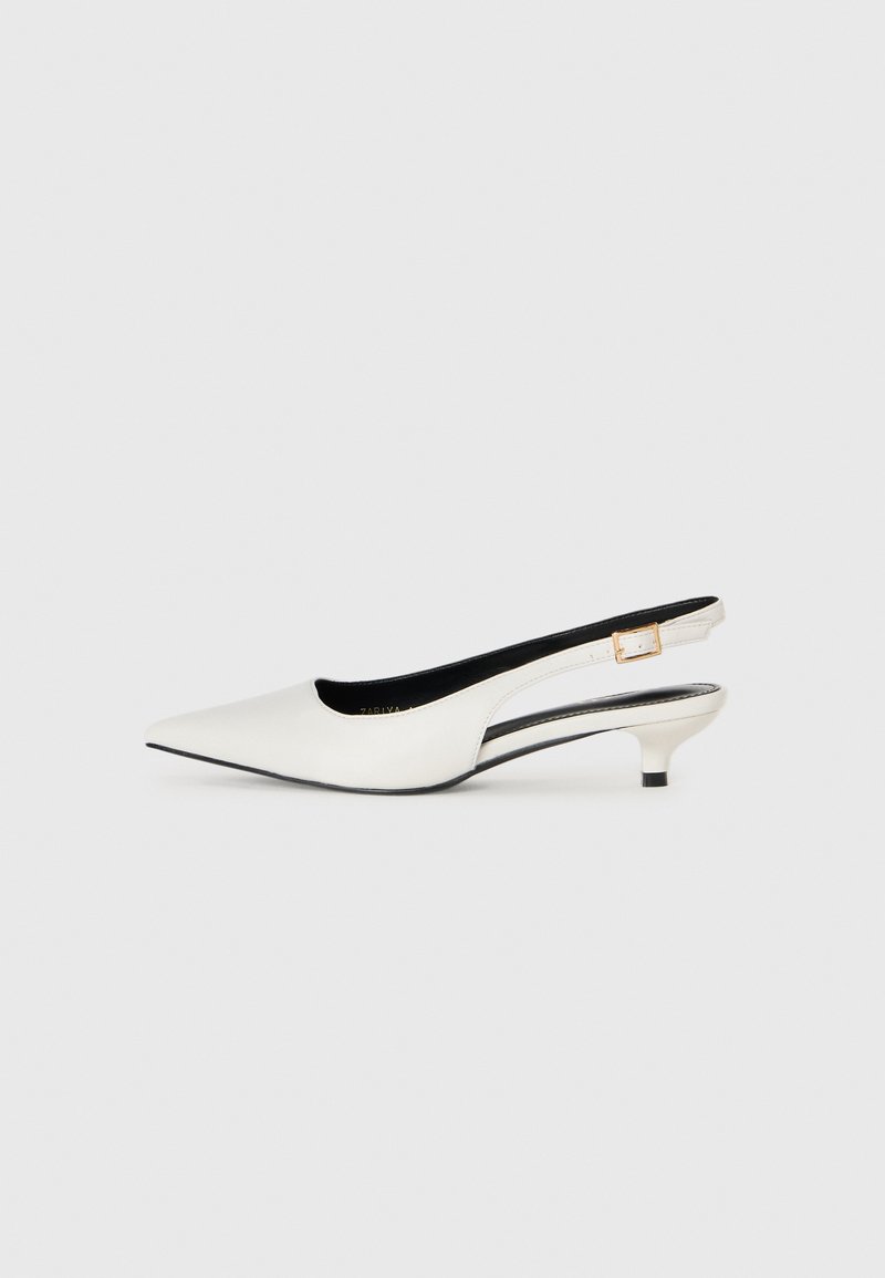 Białe skórzane buty na niskim obcasie typu slingback z wydłużonym noskiem i złotą klamrą na jednolitym jasnym tle.