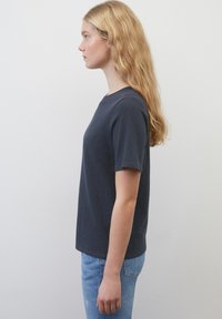 T-shirt bleu marine à manches courtes en tissu doux, col ras du cou, coupe décontractée, associé à un jean bleu clair, présenté de côté sur un fond uni.