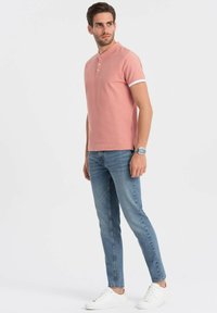 Světle růžová polo košile s bílými detaily, s henley límcem a třemi knoflíky, kombinovaná s úzkými modrými džíny a bílými teniskami.