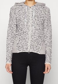 Texturerad zip-up hoodie i vitt och grått med ett luddigt yttre, grå huva och sidospår. Utrustad med dragsnören och dragkedja framtill.