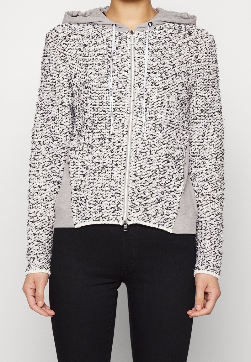 Texturerad zip-up hoodie i vitt och grått med ett luddigt yttre, grå huva och sidospår. Utrustad med dragsnören och dragkedja framtill.