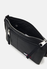 Zwarte nylon tas met ritsluiting, voorvak en leren accenten. Heeft een strak design en een verstelbare schouderband voor veelzijdigheid.