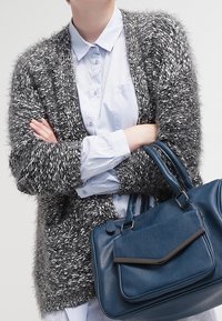 Grå och vit texturerad kofta över en ljusblå skjorta, ihop med en mörkblå läderhandväska med en framficka och två handtag.