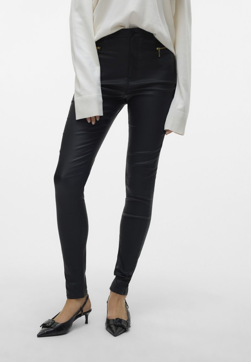 Svarta leggings i läderlook med skinny fit, hög midja och gulddragkedjor på framfickorna. Bärs med en vit oversized tröja.