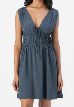 Sukienka bez rękawów w ciemnoszarym kolorze, z głębokim dekoltem w serek, wiązanym detalem z przodu i marszczoną talią, opadająca ku rozszerzanemu dołowi. Miękka faktura materiału.