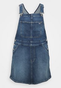 Džínová overall šaty v středně modrém odstínu. Obsahuje nastavitelné ramínka, přední kapsu, boční knoflíky a mírně rozšířený lem.