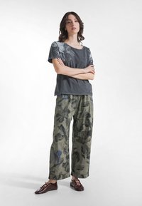 Szary t-shirt z krótkim rękawem z kwiatowym nadrukiem, zestawiony z szerokimi zielonymi spodniami w wzory oraz bordo butami sznurowanymi.