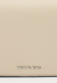 Portafoglio in pelle beige, con texture a rilievo e finitura liscia. Presenta un logo metallico "Michael Kors" nella parte inferiore.