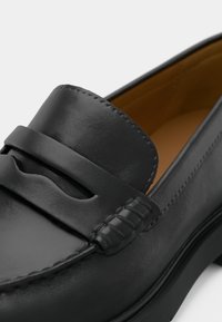 Μαύρο δερμάτινο loafer τύπου penny με ραφές moc toe και ταμπά εσωτερική επένδυση.