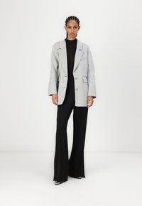 Blazer gris de gran tamaño con doble botonadura, que presenta un solapa estructurada y bolsillos inclinados, combinado con pantalones negros de pierna ancha.