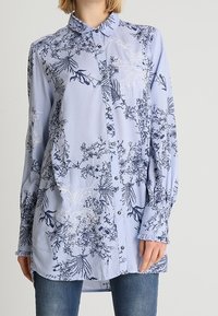Vaaleansininen napillinen paita, jossa on merkkikuosiset kukat tummansinisellä ja valkoisella. Ominaisuudet: pitkät hihat, kaulus ja rento malli. Pehmeä, tekstuuriinen kangas.