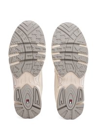 Sohlen von beigen und grauen Turnschuhen mit gemusterten Profilen und einem kleinen rechteckigen roten, weißen und blauen Logo nahe der Ferse.