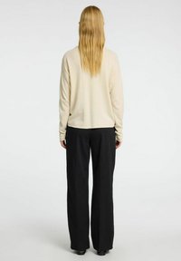Beige top s dlouhým rukávem a volným střihem, v kombinaci s kalhotami s vysokým pasem a širokými nohavicemi v černé barvě, s uniformní texturou látky a jednoduchým designem.