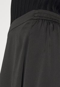 Sort ribbet top med elastisk talje og en flydende grå stofskørt nedenfor. Glat overflade, med et enkelt, rent design.