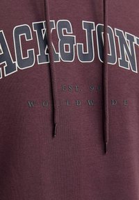 Bordo dukserica s kapuljačom i špagom, sa velikim bijelim i mornarsko plavim natpisom "BLACK&JON" i manjim sivim slovima ispod. Mekana, teksturirana tkanina.