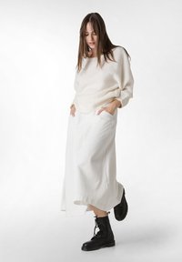 Cremefarbenes, weiches Wollpullover kombiniert mit einem langen, weißen, strukturierten Rock. Schwarze Schnürstiefel runden das Outfit ab.