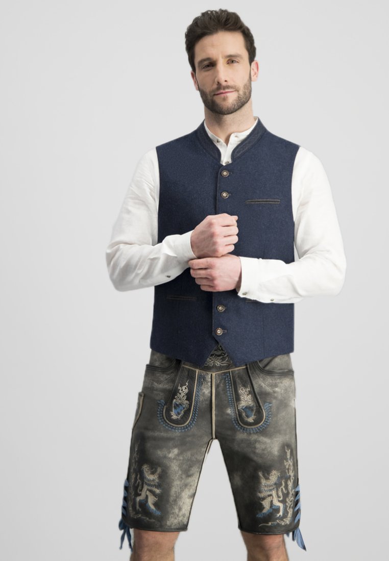 Marineblaue Wollweste mit hohem Kragen und vorderem Knopfverschluss, kombiniert mit grauen Shorts, die mit blauen bestickten Mustern und dekorativen seitlichen Fransen verziert sind.