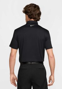 Czarna koszulka polo z kołnierzykiem, krótkim rękawem i białym logo Nike na plecach. Noszona z czarnymi spodniami i czarnym paskiem.